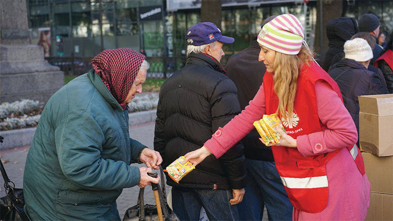 Una volontaria Caritas porge del cibo ad un'anziana sola